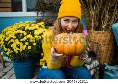 Close up, Beautiful young blond woman holding orange pumpkin in garden.