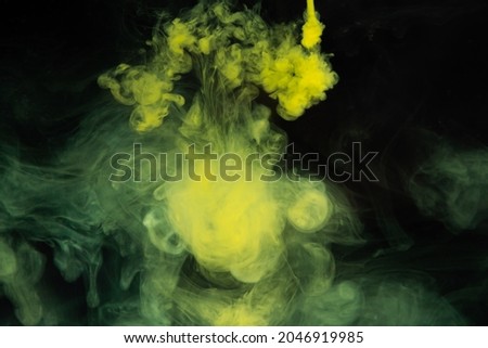 Yellow paint dissolves in water on a black background. Watercolor paint in water