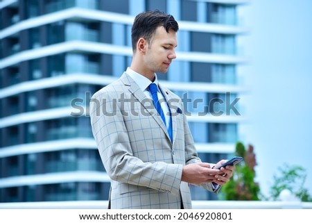 Businessman using smart phone on modern skyscraper background. Business and technology concept.