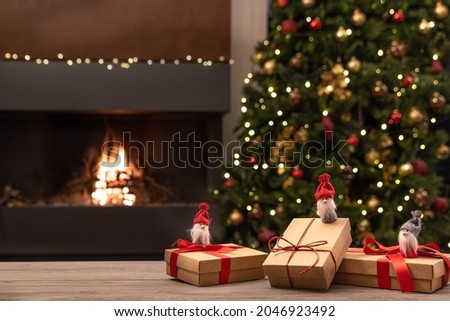 Cozy Christmas atmosphere with Christmas gnomes and gifts on wooden table. In the background blurred the fireplace with fire, the Christmas tree and Christmas decorations. Selective focus