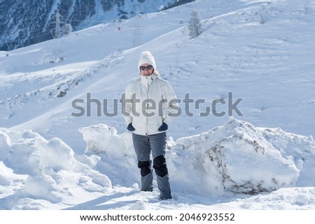 A view of a caucasian woman dressed in a skiing suit and standing in the snow on the mountain
