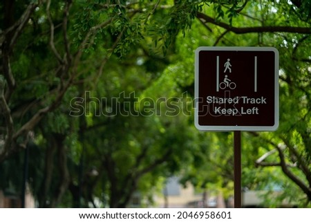 A pedestrian and cyclist shared track sign on the background of tree branches