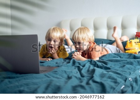 cute little caucasian kids boys twins using laptop in bed at home. Kids using technology.