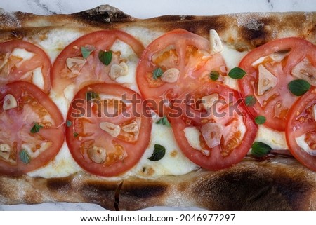 Top closeup view of a Neapolitan pizza with mozzarella cheese, sliced tomato, fresh oregano leaves and roasted garlic. 