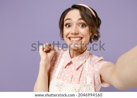 Close up overjoyed happy young housewife housekeeper chef cook baker woman wear pink apron do selfie shot on mobile phone do winner gesture isolated on pastel violet background. Cooking food concept