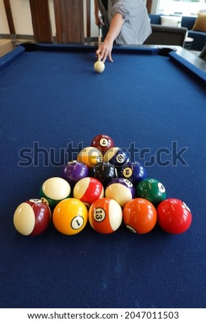 On a blue pool table, a man aims a cue at different colored billiard balls.