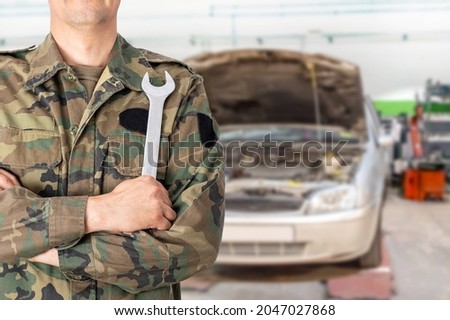 Hand of a military car mechanic with wrench. Car repair garage. Royalty-Free Stock Photo #2047027868