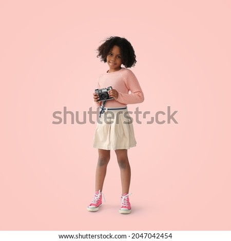 Beautiful girl smiles and holds a camera on the pink background	
