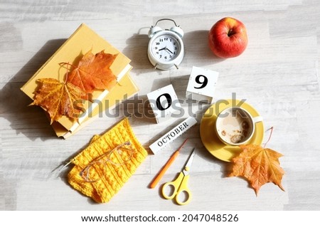 Calendar for October 9 : the name of the month in English, cubes with the numbers 0 and 9, books, alarm clock, maple leaves, red apple, knitted scarf, cup of coffee, eyeglasses on a gray background