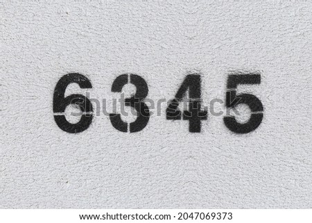Black Number 6345 on the white wall. Spray paint. Number six thousand three hundred forty five.