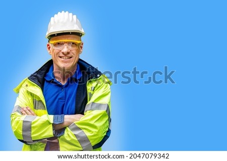 Factory engineer senior man standing confidence with green working suite dress and safety helmet. manual worker in front blue background. Concept of smart industry worker operating.