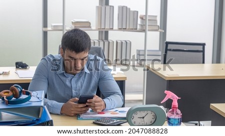 An attractive male office worker is using a smartphone to check his business and market information online. Business man use digital device to enhance his marketing. A man is chatting with his friends