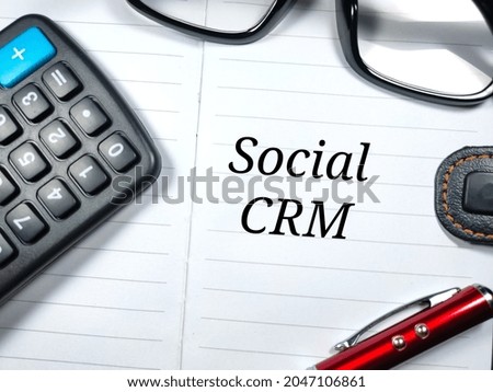 Business concept.Text Social CRM writing on notebook with pen,glasses and calculator.