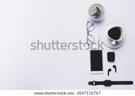 Top view, table with cactus, smartwatch, glasses, a cup of coffee, smartphone, and earphones isolated on white background.