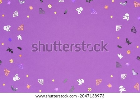 Happy Halloween concept. Frame from confetti in the form of skulls, spiders, cobwebs, bats and ghosts on a purple background. Copy space.