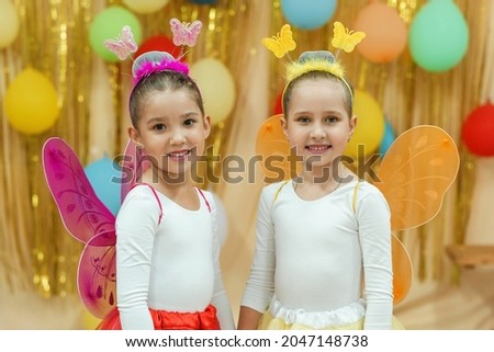 Two little girls in carnival costumes of fairy butterflies are standing on a shiny gold background with balloons. Children's theater. A dance group. Royalty-Free Stock Photo #2047148738