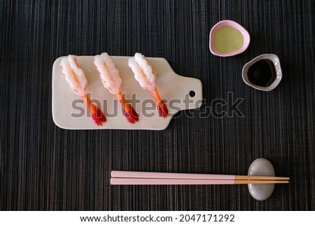 Raw Shrimp prawn sushi in japanese restaurant. Sushi - ama Ebi Nigiri on white board with chopsticks and souse on black background. High quality photo