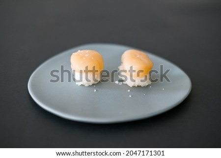 Two Nigiri Sushi with scallop in restaurant served on light-grey plate. Two sushi pieces isolated on black background. Japanese food.
