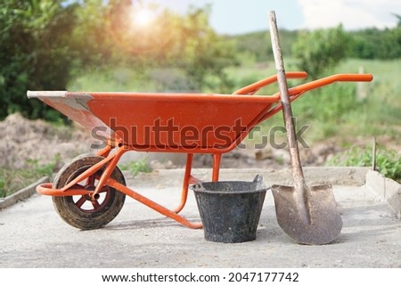 Orange wheel barrow cart trolley , bucket and shovel  that use for construction to carry cement mixture at worksite. Concept : Construction worker's  tool.                              