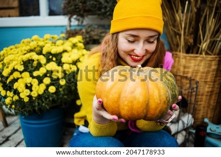 Close up, Beautiful young blond woman holding orange pumpkin in garden.