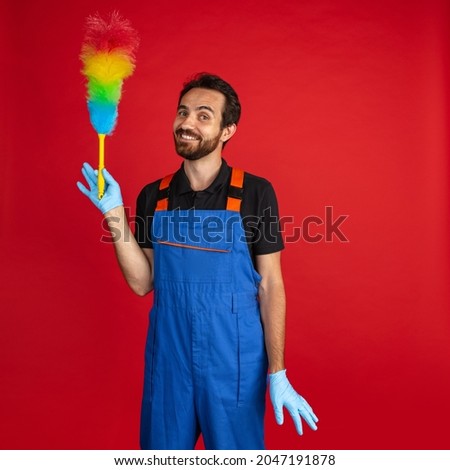 Gentle car repair. Smiling young bearded man, male auto mechanic or fitter wearing blue work dungarees isolated over red studio background. Concept of funny meme emotions, ad, job, insipation, ideas Royalty-Free Stock Photo #2047191878