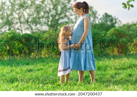little girl kisses pregnant mom in the belly. in expectation of a child, taking care of children.