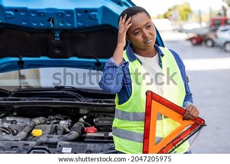 Young female driver wearing a high visibility vest-safety vest, putting in place the warning triangle after her car has broken down. Help on the road concept. 