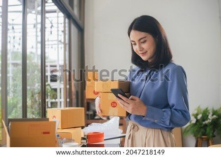Business woman owner holding parcel box for delivery and using smartphone at home office. Entrepreneur small business working at home. Royalty-Free Stock Photo #2047218149