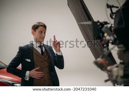 Professional male actor works in the frame on the set. Shooting with a car on a large white cyclorama. Handsome young man on the set of a movie, commercial or TV series. Filming indoors, studio