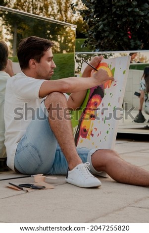 male artist paints his portrait in the park on the asphalt reflection in the mirror in warm autumn shades