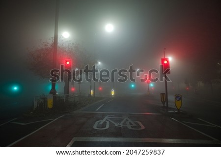 Colored traffic lights and white street lights shine through thick night time fog at a road junction near the hallamshire hospital in sheffield.