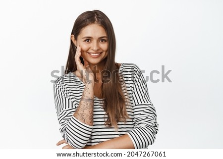 Adult woman smiling, touching her face and looking happy, posing against white background