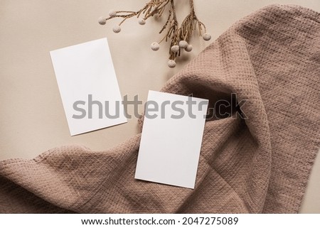 Blank paper sheet card with mockup copy space and dry floral branch and blanket cloth on neutral beige background. Minimal aesthetic business brand template. Flat lay, top view