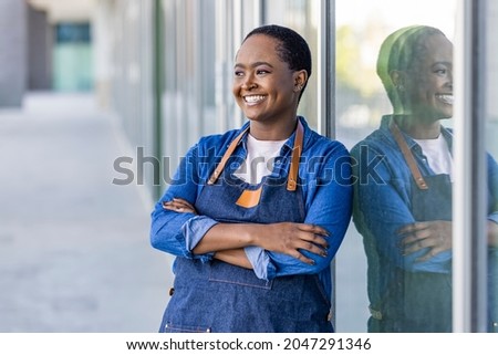 Portrait of a happy waitress standing at restaurant entrance. Portrait of business womanattend new customers in her coffee shop. Happy woman owner showing open sign in her small business shop.