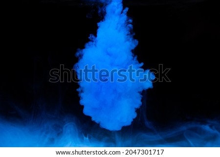 Blue paint dissolves in water on a black background. Watercolor paint in water