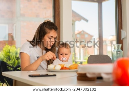 Beautiful mother is trying to feed her baby girl while the baby is having a pacifier in her mouth
