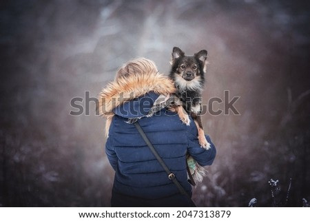 A cute mixed breed dog sitting on the shoulder of a girl in a blue coat on the background of a winter fairy forest. Looking into the camera. Family portrait
