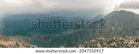 Panorama from a rocky ridge to a valley with silhouettes of mountains against a background of cumulus clouds
