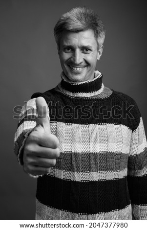 Studio shot of man with blond hair wearing turtleneck sweater against gray background in black and white