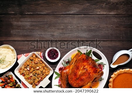 Traditional Thanksgiving turkey dinner. Top view bottom border on a dark rustic wood background with copy space. Turkey, mashed potatoes, dressing, pumpkin pie and sides.