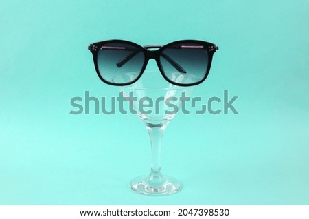 Cocktail glass with sunglasses on blue background. Creative idea. Minimal party concept, layout