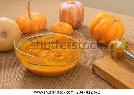 Pumpkin puree in a glass bowl, fresh pumpkin, squash, butternut close up on kitchen table