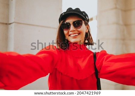 Portrait of wonderful white female model with bright fashion look expressing energy in good day in Europe. Lovely happy woman in stylish hat making selfie while walking past old building.