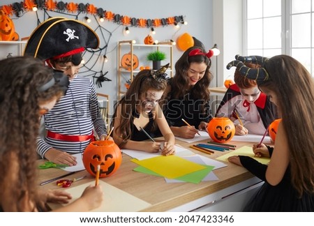 Arts and Crafts studio teacher doing creative activity with kids. Children dressed up as pirates, witches and vampires having fun Halloween party with their young English tutor at after school club
