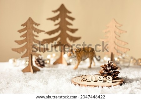 New year 2022. Numbers 2022 on wooden stand on beige pastel blurred background with decorative tiger, fir trees, snow and lights. Christmas greeting card.