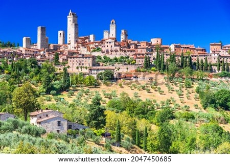San Gimignano medieval town skyline and famous towers sunny day. Italian olive trees in foreground. Tuscany, Italy, Europe.