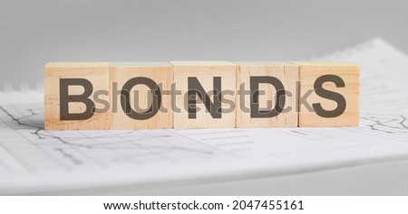 bonds is written on light wooden blocks. the word is located on a sheet with charts and graphs. business concept. gray background