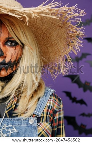Cropped close up shot young woman with Halloween makeup mask in straw hat scarecrow costume point on face paint body art isolated on plain dark purple background studio. Celebration holiday concept.