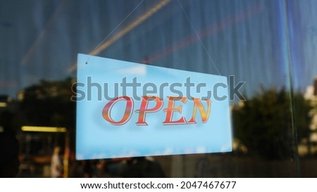Open text on signboard hanging on rope behind glass door of shop or restaurant outdoor