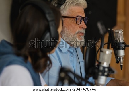 a European couple, a man and a woman, record a podcast or broadcast on the radio. a man and a woman in a recording studio with microphones and headphones create audio content. podcasters I'm recording